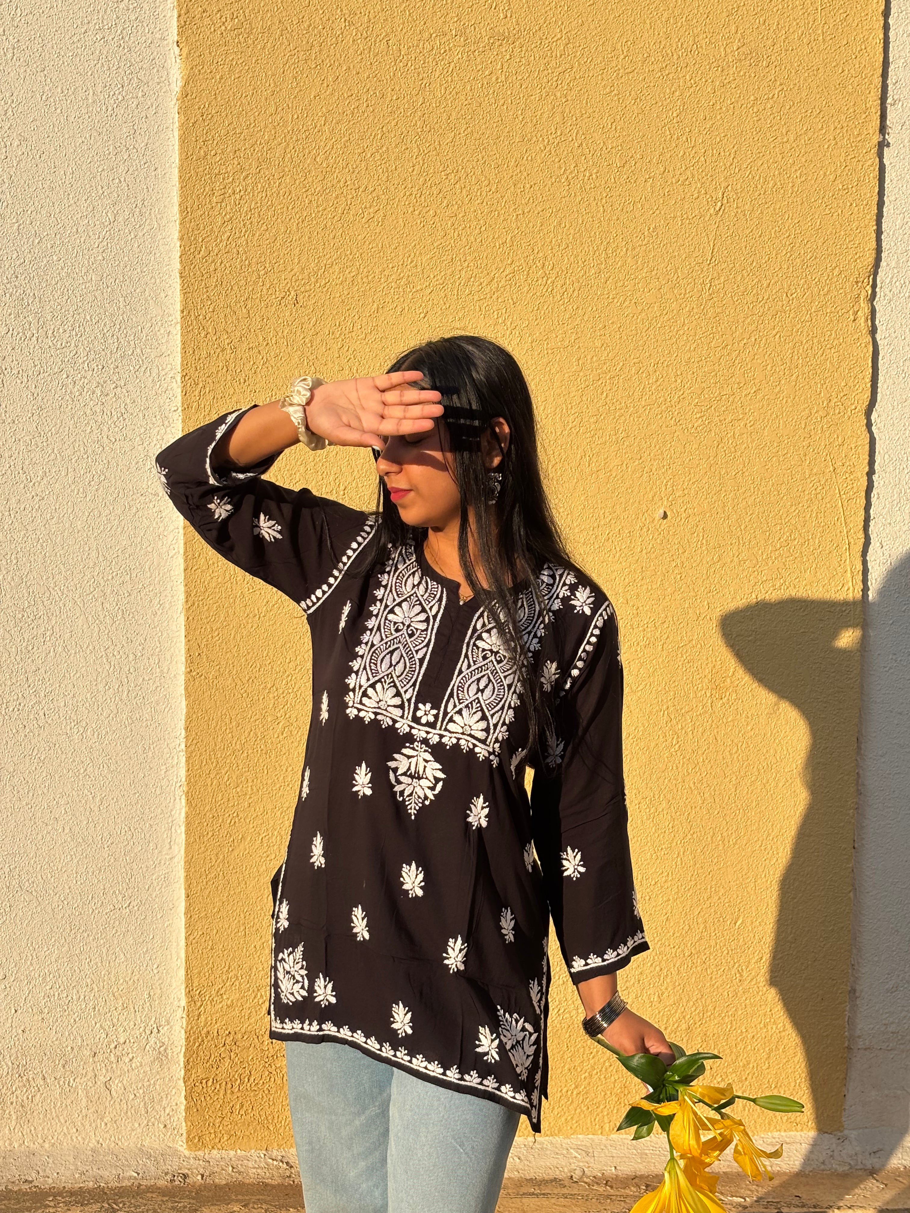 Woman in a black patterned top standing against a yellow wall