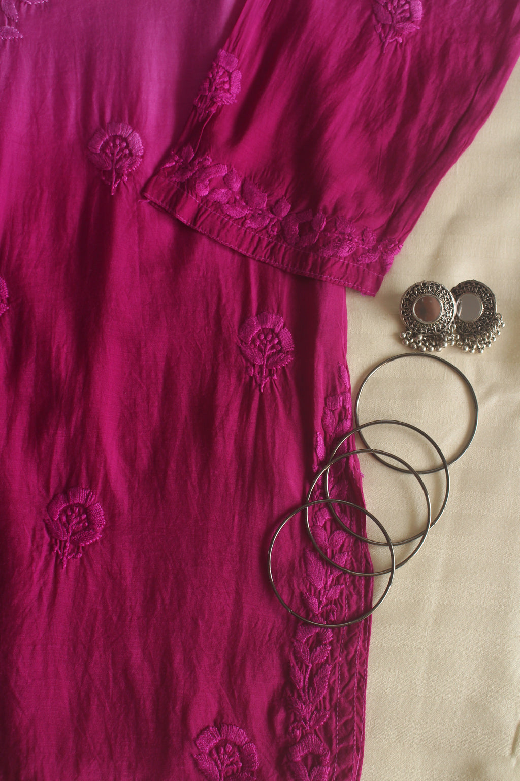 Pink embroidered garment with black hair ties on a beige background